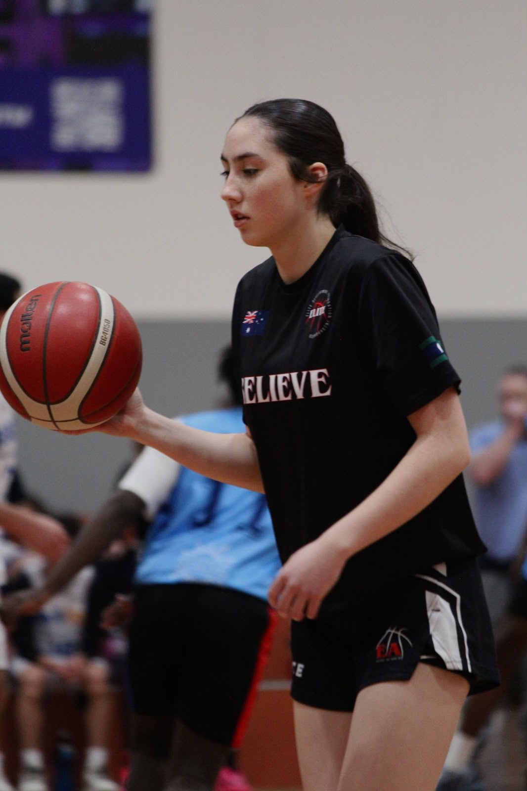 A player in an El!te Believe warm-up shirt with a ball